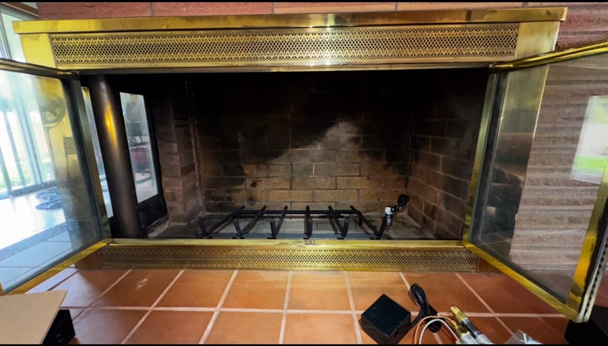 Open brass fireplace doors revealing a masonry firebox and log grate