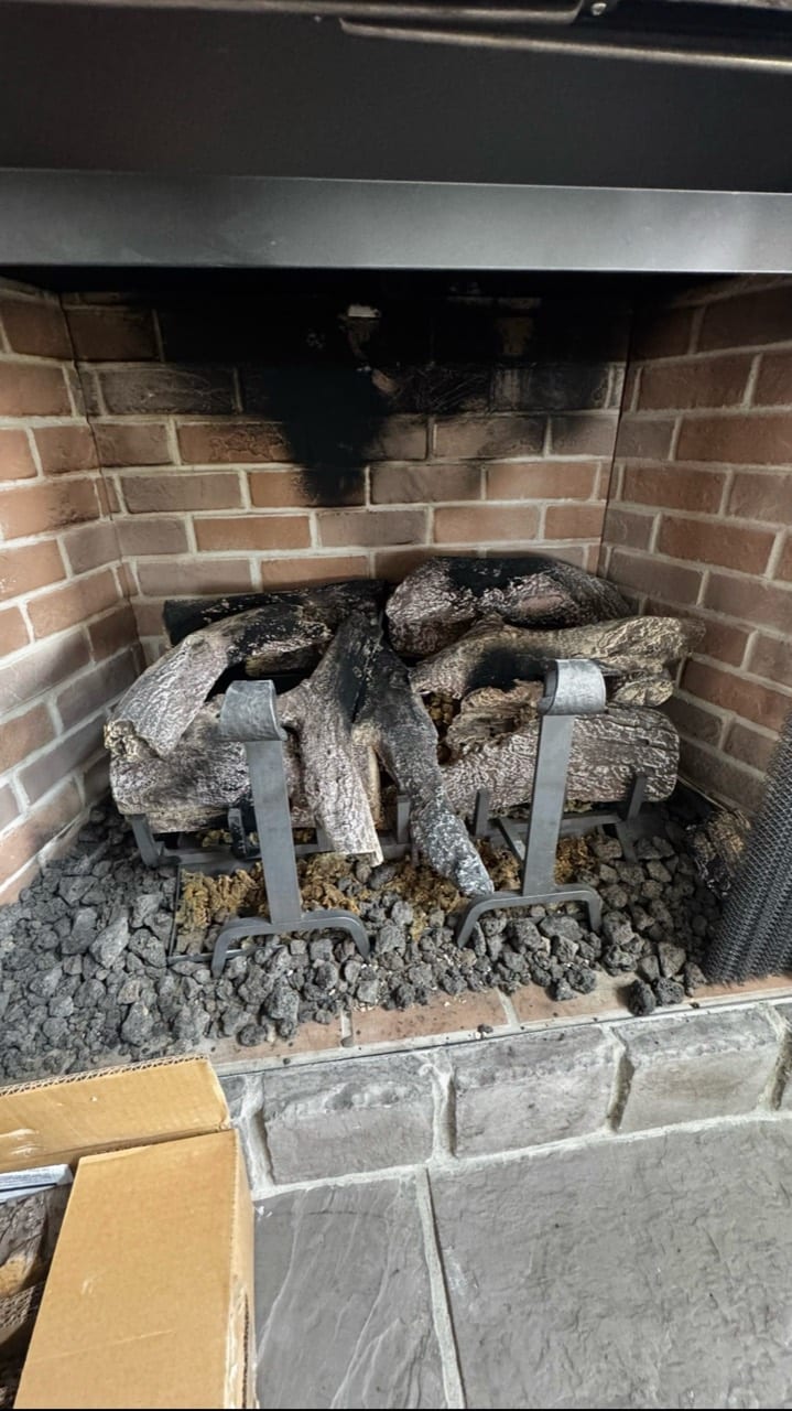 Gas logs resting in a brick fireplace with a black metal surround